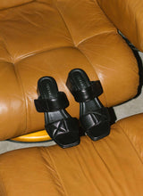 Lade das Bild in den Galerie-Viewer, Elegant-alltagstaugliche Absatzsandale aus schwarzem Leder mit Karreefront auf einem cognacfarbenen Ledersessel