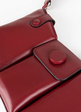 Lade das Bild in den Galerie-Viewer, Detailfoto einer dunkelroten Crossbody-Bag aus weich gepolstertem Glattleder mit drei voneinander abgetrennten Fächern und einem farblich passenden, breiten Gurt aus Leder mit Karabinerhaken