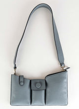 Lade das Bild in den Galerie-Viewer, Produktfoto einer grauen Crossbody Tasche, deren Kalbsleder in einem hellen Kieselgrau gehalten ist. Die Oberfläche weist eine dezent körnige Narbung auf, aus diesem Grund trägt die Handtasche unter anderem den Beinamen "pebbled". Weiterhin wird sie von den Gründerinnen der Marke auch als Toolbag bezeichnet, da es sich um ein praktisches Format handelt und in den drei Fächern alles Notwendige untergebracht werden kann. Die Marke ist CEDOUBLÉ.