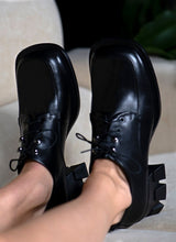 Lade das Bild in den Galerie-Viewer, Bild eines schwarzen Schnürers für Damen mit exzentrischem Karree Leisten, silberfarbenen Hakenösen und einem skulpturalen Absatz mit breiter Auftrittsfläche.