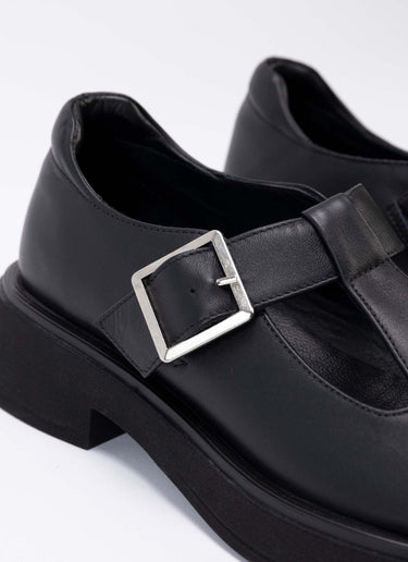 Detailaufnahme eines schwarzen Mary Jane Schuhs mit einer Laufsohle mit leichtem Plateau. Abgerundet wird der Schulmädchen-Look durch eine silberfarbene Schnalle. Obermaterial und Futter sind aus weichem, schwarzem Echtleder.