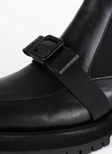 Load image into Gallery viewer, Detailfoto eines schwarzen Chelseaboots aus Leder von CEDOUBLÉ mit dekorativer Schnalle in Schleifenoptik, die sich mit einem elastischen Band über den Spann schmiegt.
